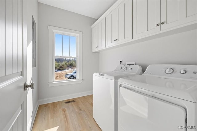 clothes washing area featuring separate washer and dryer, cabinets, and light hardwood / wood-style floors