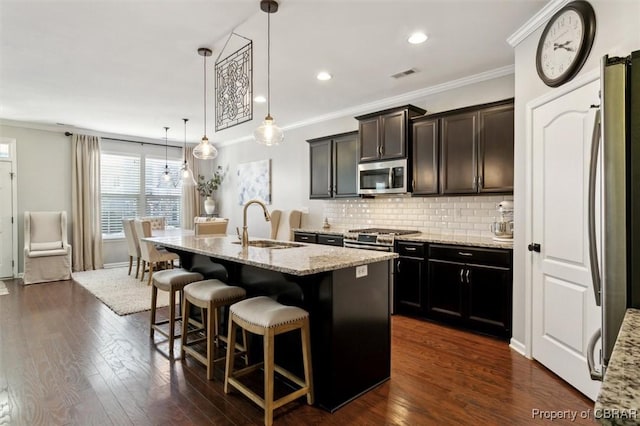 kitchen with stainless steel appliances, decorative light fixtures, a kitchen breakfast bar, an island with sink, and light stone countertops