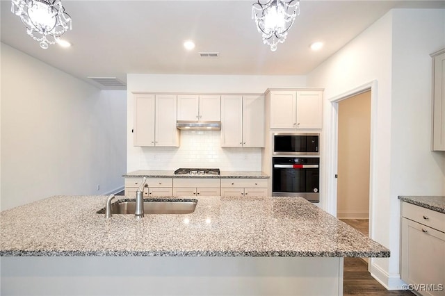 kitchen with light stone counters, a center island with sink, appliances with stainless steel finishes, and sink