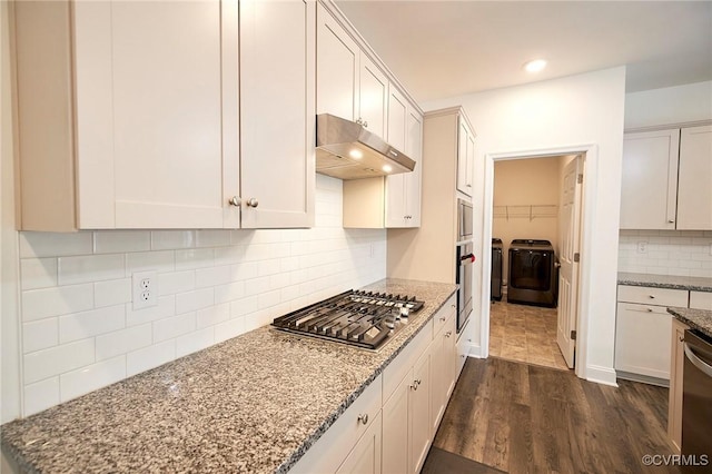 kitchen with stainless steel appliances, washing machine and clothes dryer, white cabinetry, decorative backsplash, and dark wood-type flooring