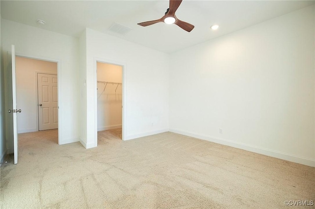 unfurnished bedroom featuring a walk in closet, light colored carpet, ceiling fan, and a closet