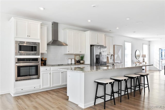 kitchen with white cabinets, stainless steel appliances, a kitchen island with sink, and wall chimney exhaust hood