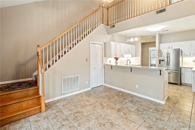 kitchen featuring light stone countertops, kitchen peninsula, white cabinets, and stainless steel refrigerator with ice dispenser