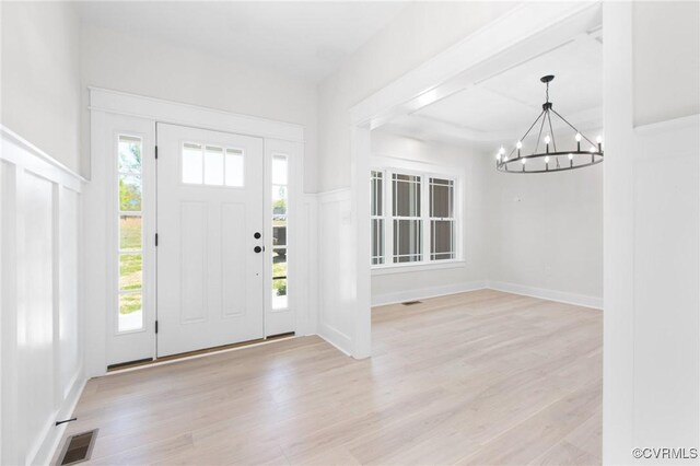 entrance foyer featuring light wood-style floors, visible vents, and an inviting chandelier