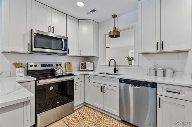 kitchen featuring light stone counters, pendant lighting, stainless steel appliances, white cabinetry, and sink