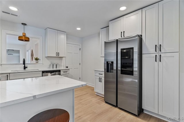 kitchen with sink, white cabinetry, light hardwood / wood-style flooring, pendant lighting, and appliances with stainless steel finishes