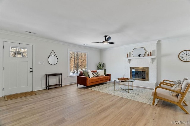 living room featuring a brick fireplace, ceiling fan, light wood-type flooring, and crown molding