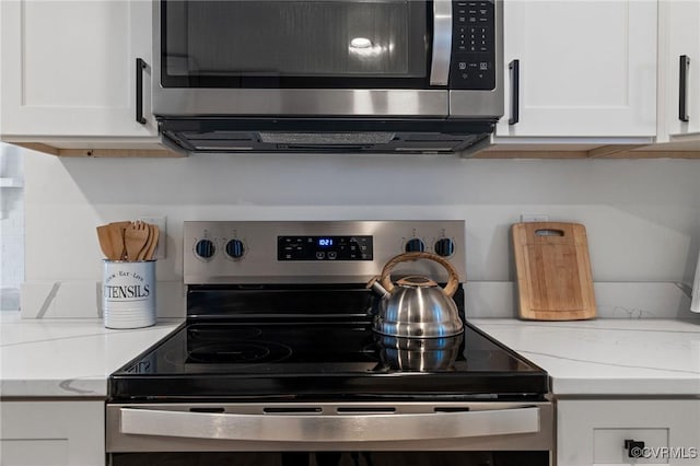 details with stainless steel appliances, light stone countertops, and white cabinetry