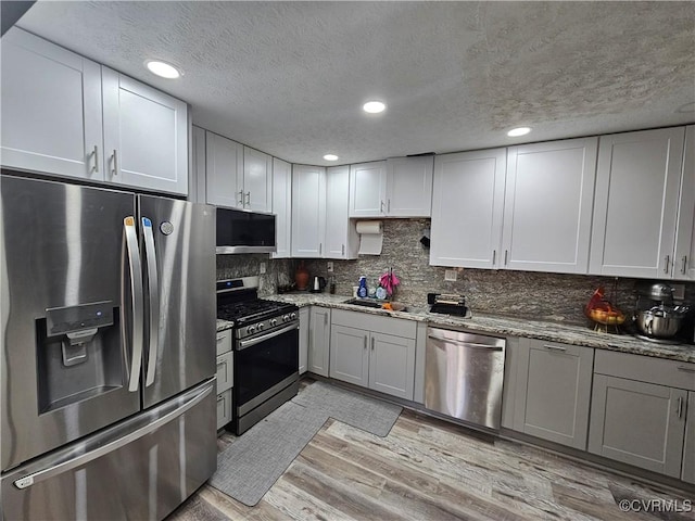 kitchen featuring light stone countertops, a textured ceiling, light hardwood / wood-style floors, and appliances with stainless steel finishes