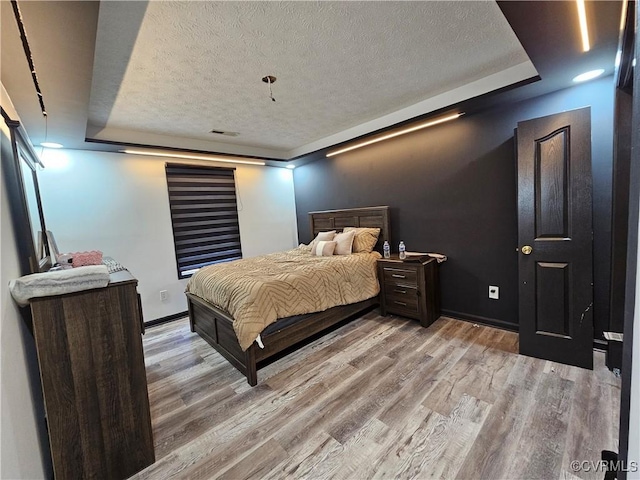 bedroom featuring a textured ceiling, a tray ceiling, and light hardwood / wood-style flooring