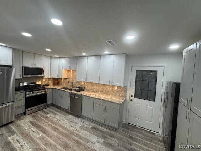 kitchen featuring sink, light wood-type flooring, backsplash, gray cabinets, and stainless steel appliances