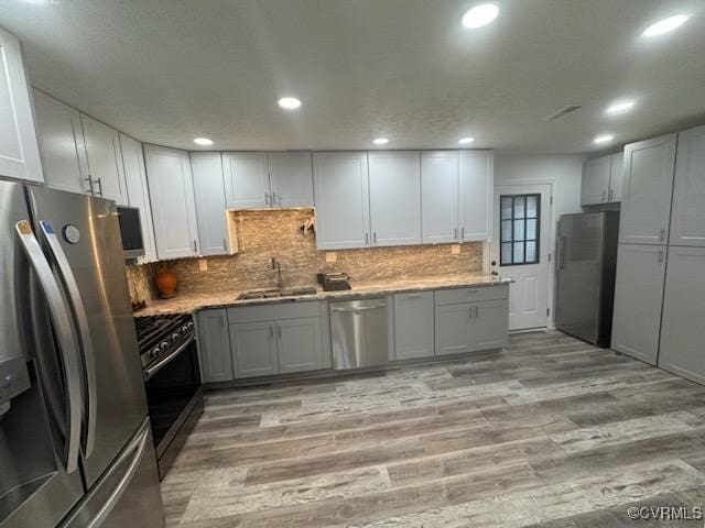 kitchen featuring light wood-style floors, appliances with stainless steel finishes, decorative backsplash, and a sink