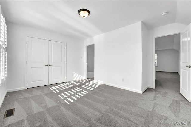 unfurnished bedroom with vaulted ceiling, light colored carpet, and a closet