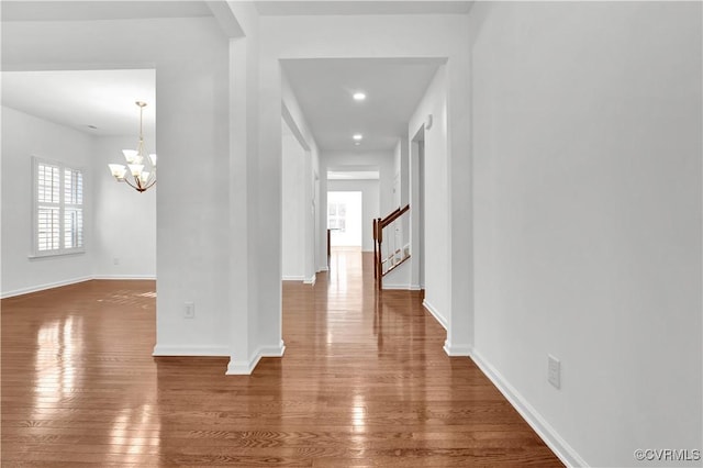 hallway with dark wood-type flooring and an inviting chandelier