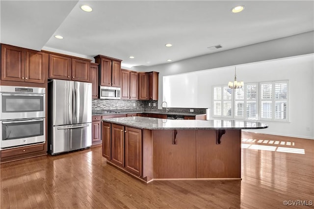 kitchen with stainless steel appliances, kitchen peninsula, dark hardwood / wood-style flooring, a kitchen bar, and an inviting chandelier