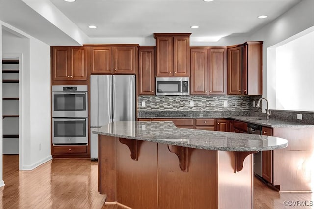 kitchen with sink, dark stone countertops, light hardwood / wood-style floors, a breakfast bar area, and appliances with stainless steel finishes