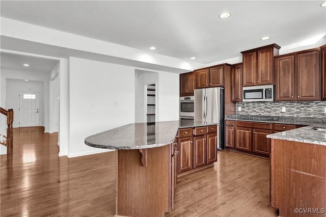 kitchen featuring stainless steel appliances, a center island, decorative backsplash, dark stone counters, and a breakfast bar