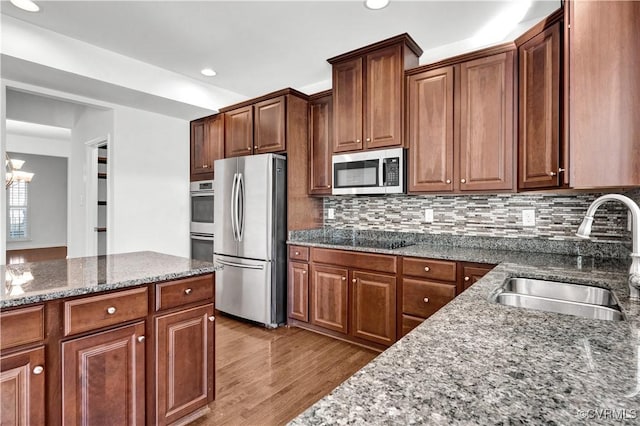 kitchen with sink, stone counters, decorative backsplash, a notable chandelier, and appliances with stainless steel finishes