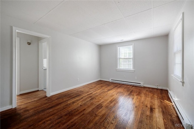 unfurnished room featuring baseboard heating, dark hardwood / wood-style flooring, and a drop ceiling