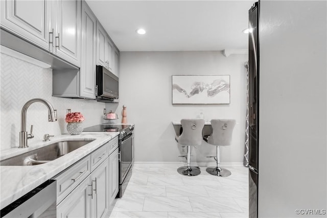 kitchen with sink, light stone countertops, decorative backsplash, gray cabinets, and appliances with stainless steel finishes