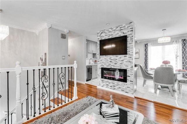 living room featuring sink, an inviting chandelier, a large fireplace, light hardwood / wood-style flooring, and crown molding