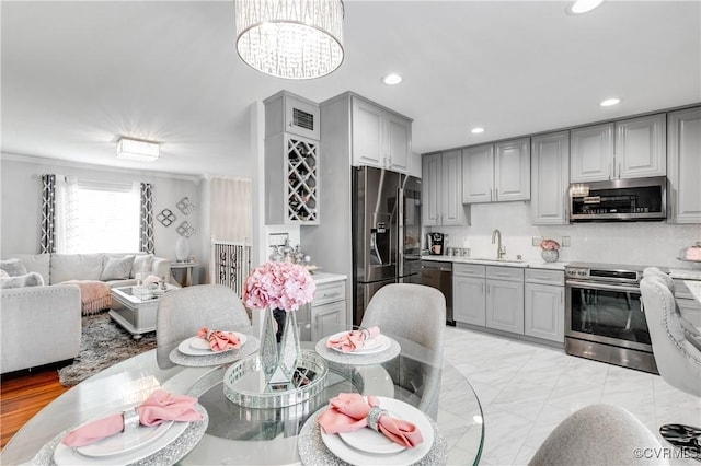 kitchen featuring gray cabinets, a chandelier, stainless steel appliances, crown molding, and decorative backsplash