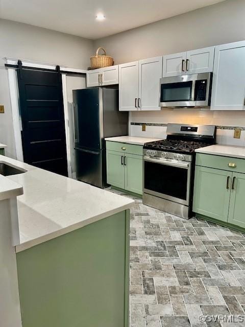 kitchen featuring green cabinets, white cabinetry, decorative backsplash, a barn door, and appliances with stainless steel finishes