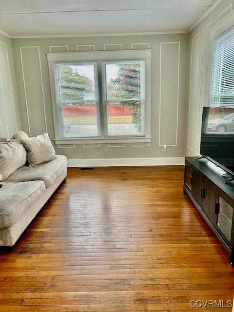 living room featuring wood-type flooring, crown molding, and a healthy amount of sunlight