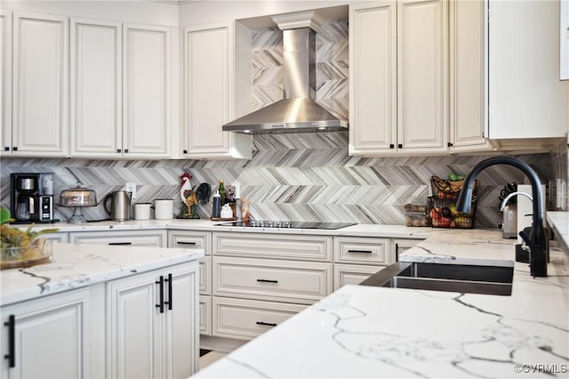 kitchen featuring light stone counters, wall chimney exhaust hood, black electric stovetop, backsplash, and sink