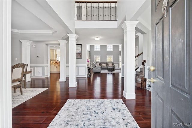 foyer entrance with dark wood-type flooring, ornamental molding, and decorative columns