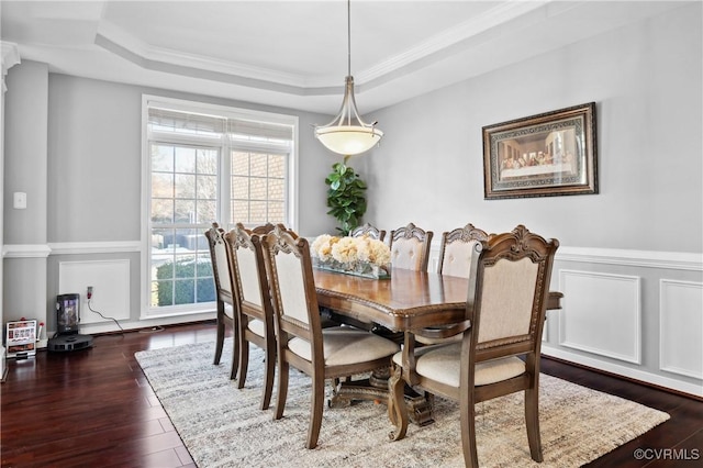 dining space featuring dark wood-type flooring, a raised ceiling, and ornamental molding