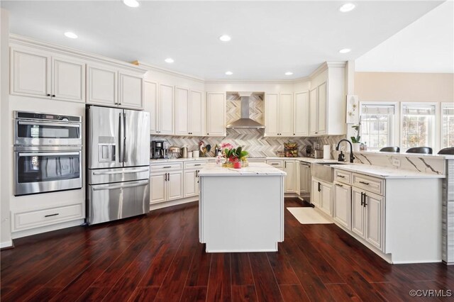 kitchen featuring light stone counters, wall chimney exhaust hood, a center island, dark hardwood / wood-style flooring, and appliances with stainless steel finishes