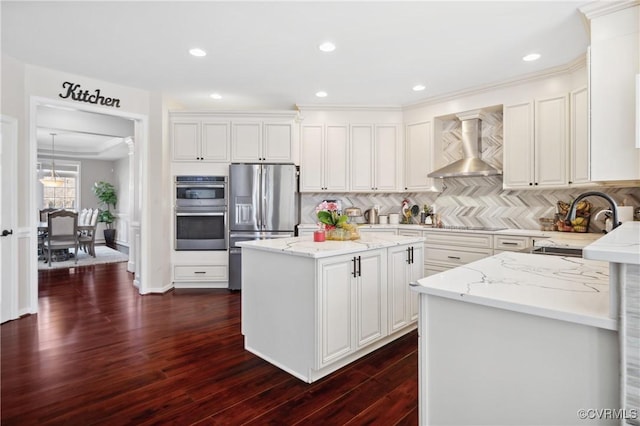 kitchen with white cabinets, a center island, backsplash, wall chimney range hood, and appliances with stainless steel finishes