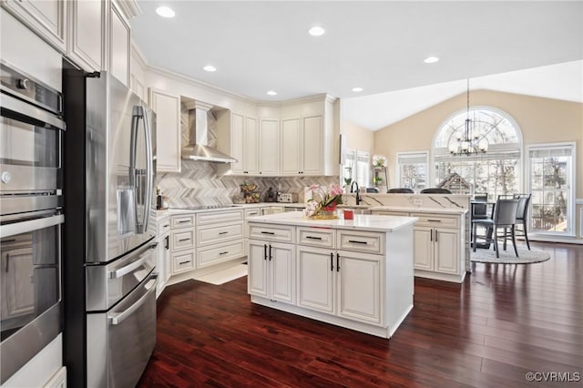 kitchen with kitchen peninsula, wall chimney exhaust hood, pendant lighting, lofted ceiling, and appliances with stainless steel finishes