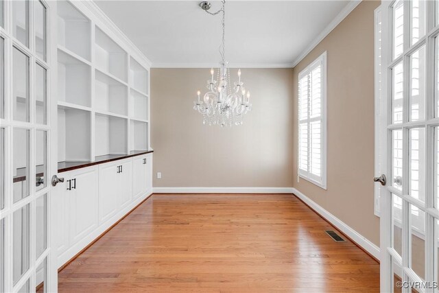 unfurnished dining area featuring light hardwood / wood-style floors, french doors, a chandelier, and ornamental molding