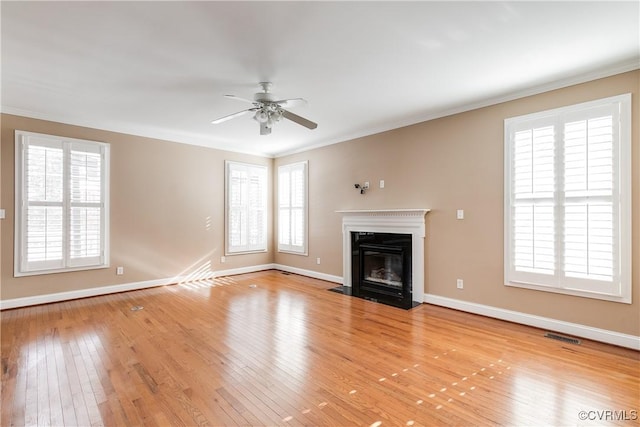 unfurnished living room featuring light wood-style floors, plenty of natural light, ornamental molding, and a fireplace with flush hearth