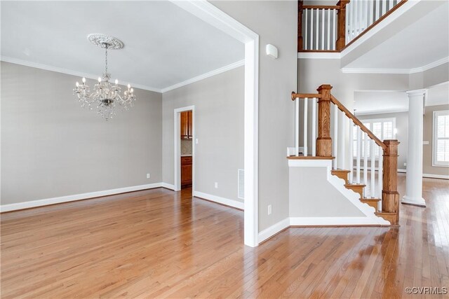 spare room featuring decorative columns, light hardwood / wood-style flooring, crown molding, and an inviting chandelier