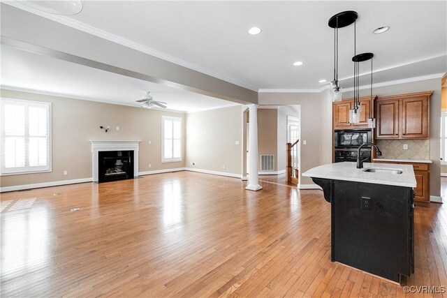 kitchen featuring a center island with sink, ceiling fan, backsplash, black microwave, and sink