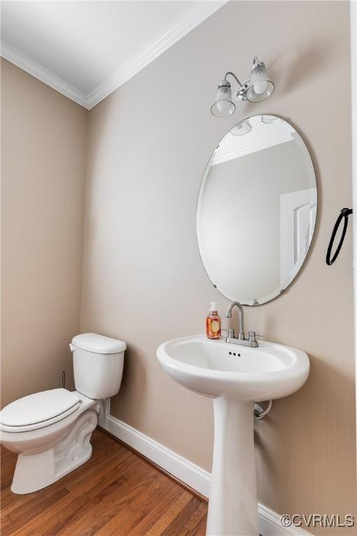 half bath featuring toilet, a sink, wood finished floors, baseboards, and ornamental molding