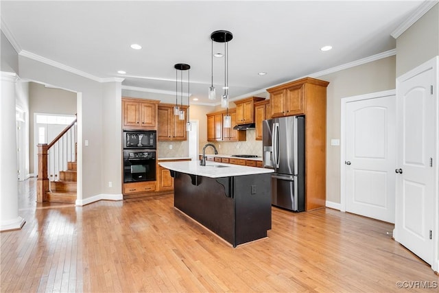 kitchen featuring pendant lighting, a breakfast bar area, light countertops, a kitchen island with sink, and black appliances