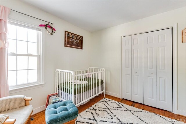 bedroom featuring hardwood / wood-style floors, a nursery area, a closet, and multiple windows