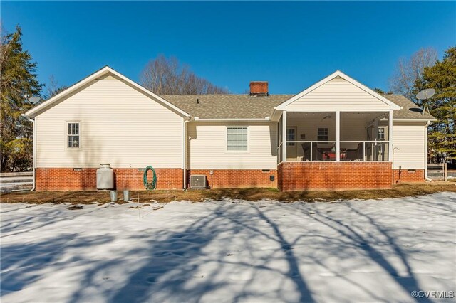 snow covered house with central AC unit and a sunroom