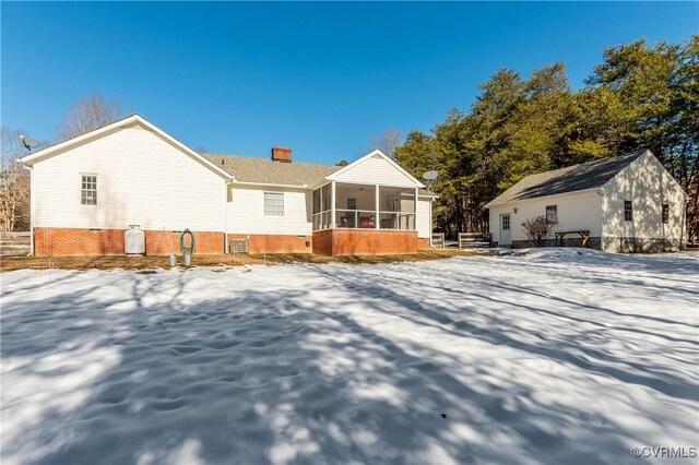 snow covered rear of property featuring a sunroom