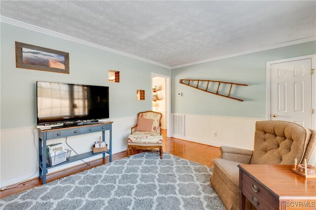 living area with hardwood / wood-style flooring, a textured ceiling, and ornamental molding