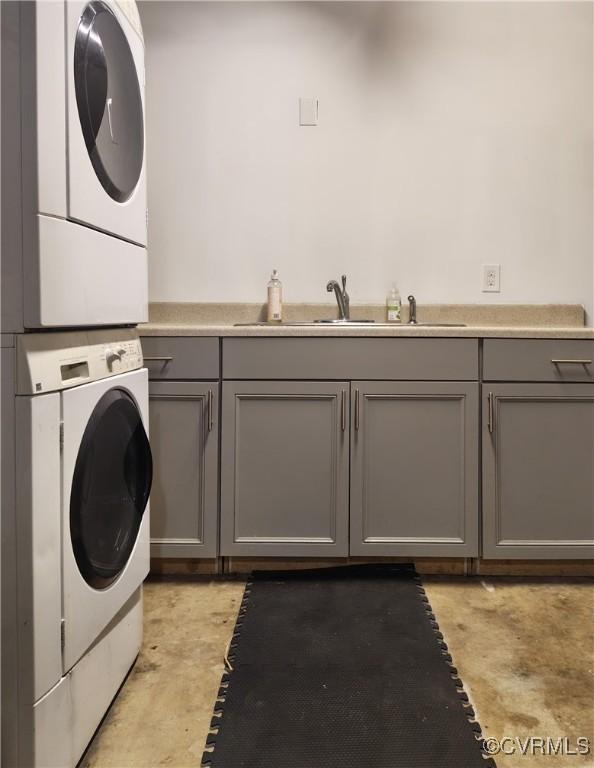clothes washing area with stacked washer / drying machine, cabinet space, and a sink