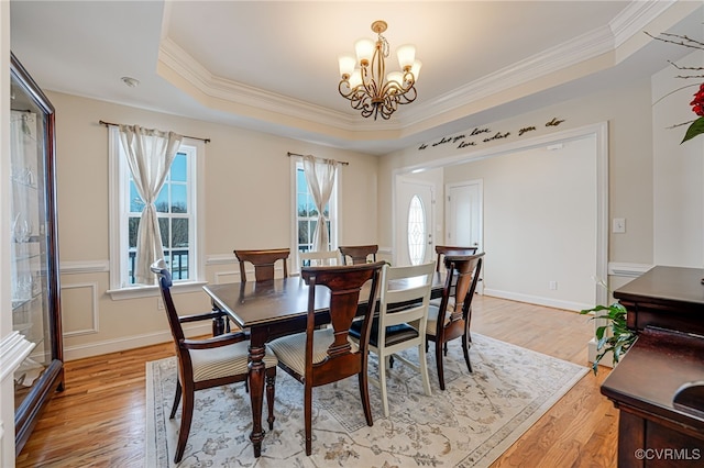 dining space featuring a raised ceiling, light hardwood / wood-style floors, crown molding, and an inviting chandelier