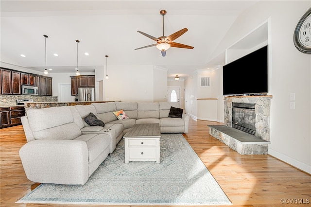 living room featuring ceiling fan, light hardwood / wood-style floors, a stone fireplace, and vaulted ceiling