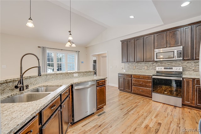 kitchen with appliances with stainless steel finishes, hanging light fixtures, light stone countertops, dark brown cabinetry, and sink