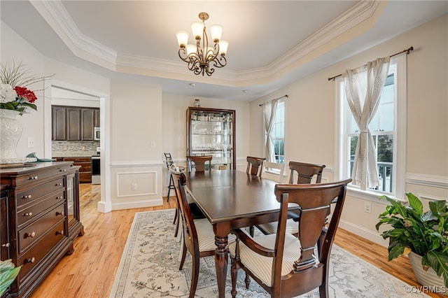 dining room with crown molding, a raised ceiling, light hardwood / wood-style flooring, and an inviting chandelier