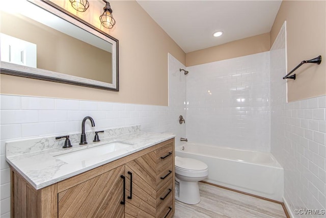 full bathroom featuring hardwood / wood-style floors, tile walls, tiled shower / bath combo, vanity, and toilet